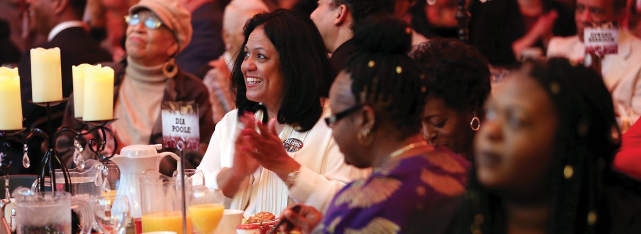 Woman in attendance claps at table with other attendees. 